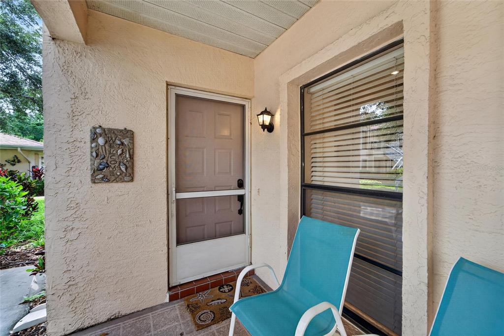 A covered patio features a screen door, a window with blinds, and two teal chairs — 319 KNOTTWOOD COURT UNIT 2, SUN CITY CENTER, FL