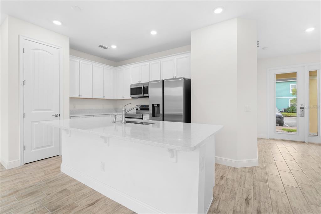 A modern kitchen features white cabinetry, stainless steel appliances, a quartz island, and tile flooring — 3069 CARIBBEAN SOUL DRIVE, KISSIMMEE, FL