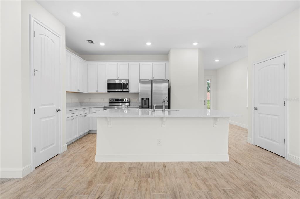A modern kitchen features white cabinetry, stainless steel appliances, a center island, and wood-look flooring — 3069 CARIBBEAN SOUL DRIVE, KISSIMMEE, FL