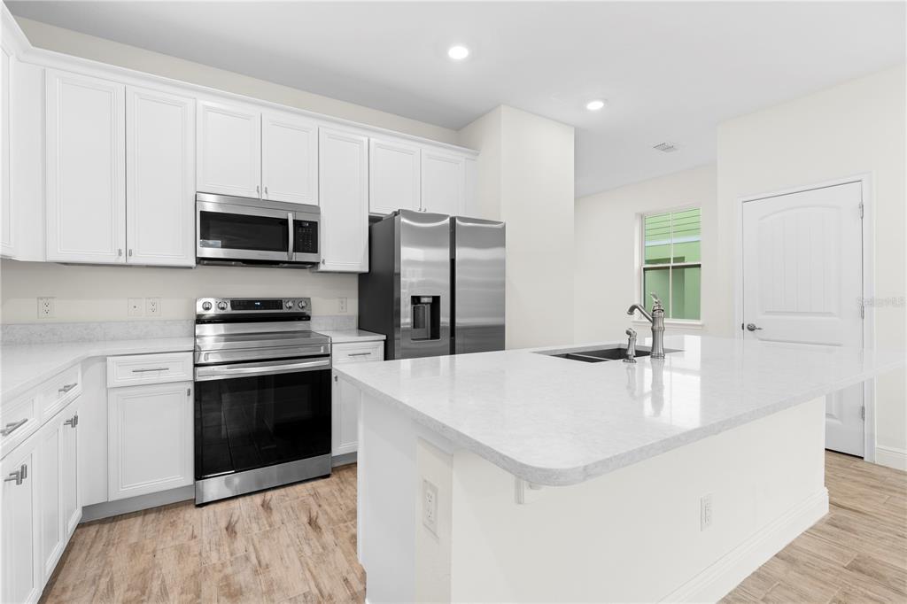 A modern kitchen features white cabinets, stainless steel appliances, and a large quartz-topped island — 3069 CARIBBEAN SOUL DRIVE, KISSIMMEE, FL