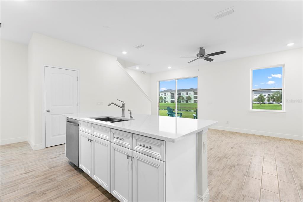 A kitchen island with white cabinets and quartz countertops overlooks a living area with tile floors — 3069 CARIBBEAN SOUL DRIVE, KISSIMMEE, FL