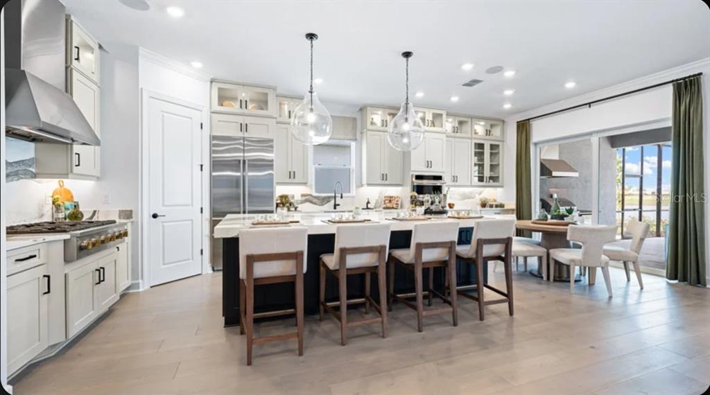 A modern kitchen features a large dark island, light cabinetry, stainless steel appliances, and pendant lighting — 10535 ECLIPSE STREET, SARASOTA, FL
