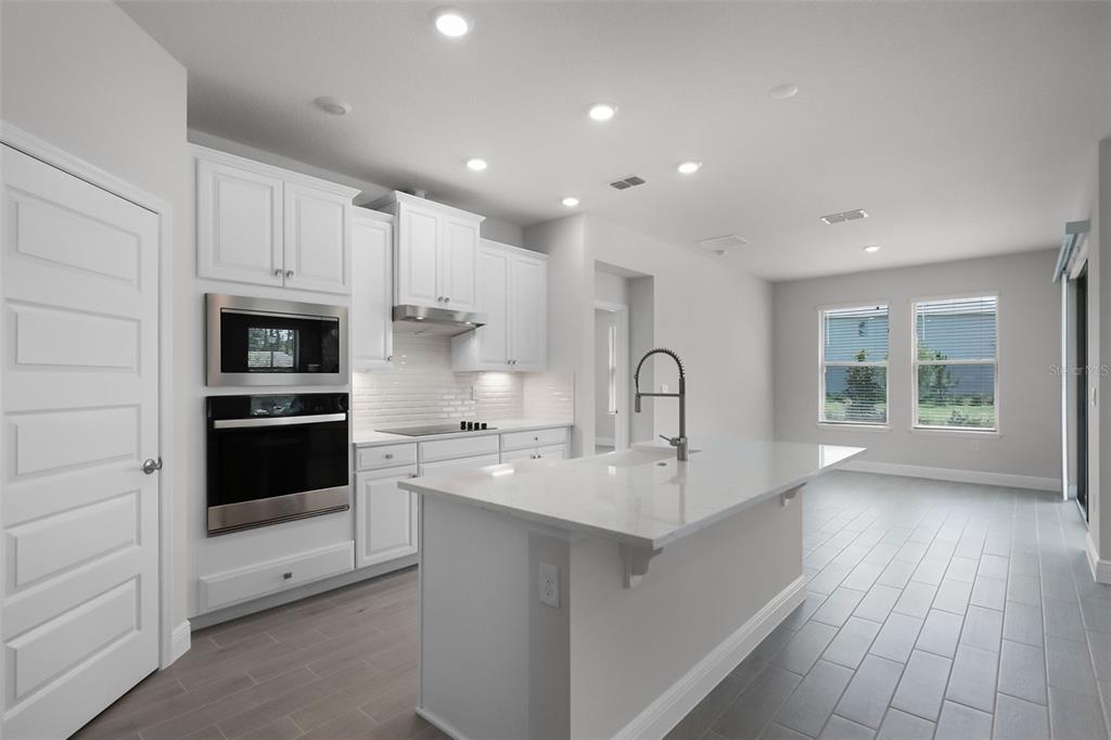 A modern kitchen features white cabinets, stainless steel appliances, a quartz island, and tile flooring — 11923 SHINE VIEW LANE, WINTER GARDEN, FL