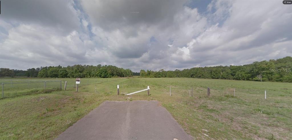 A paved driveway leads to a fenced, grassy field bordered by a line of trees — DOUBLE DIAMOND DR, POLK CITY, FL