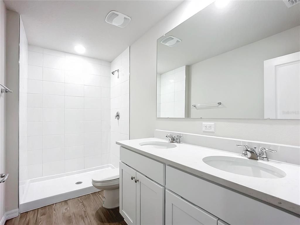 A bathroom features a double vanity with white cabinets, a large mirror, and a walk-in shower — 54 UNDERWOOD TRAIL, PALM COAST, FL