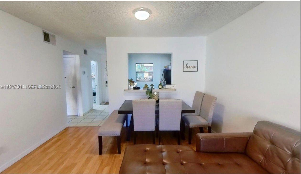 A dining area with a wooden table, chairs, and a bench sits near a kitchen pass-through — 18111 NW 68th Ave # F210, Hialeah FL 33015, HIALEAH, FL