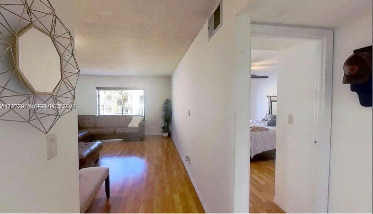 A living room with hardwood floors leads to a bedroom through an open doorway — 18111 NW 68th Ave # F210, Hialeah FL 33015, HIALEAH, FL