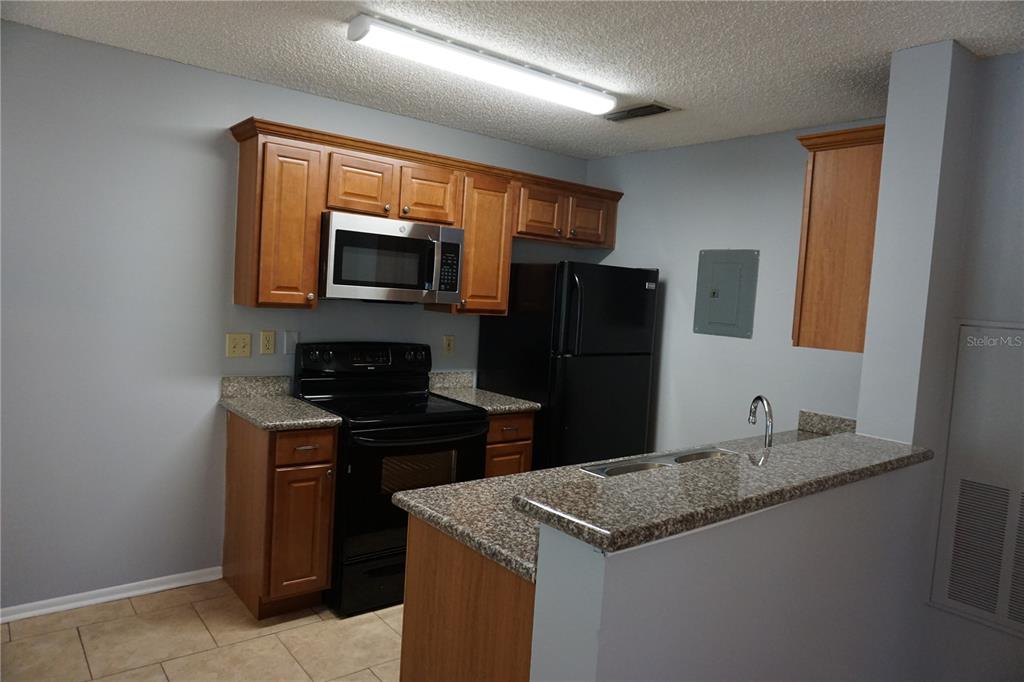 A kitchen features wood cabinets, black appliances, granite countertops, and a breakfast bar — 732 SECRET HARBOR LANE UNIT 100, LAKE MARY, FL