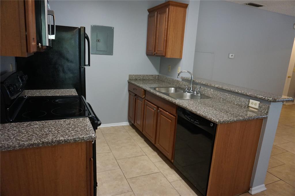 A kitchen features wood cabinets, granite countertops, black appliances, and light-colored tile flooring — 732 SECRET HARBOR LANE UNIT 100, LAKE MARY, FL