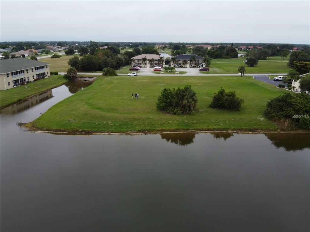 An aerial view shows a vacant grassy lot situated between a pond and apartment buildings — 26253 & 26263 NADIR ROAD, PUNTA GORDA, FL