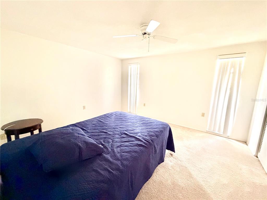 A bedroom features a blue bedspread, a ceiling fan, and two windows with vertical blinds — 7016 CUTTY SARK DRIVE, PORT RICHEY, FL
