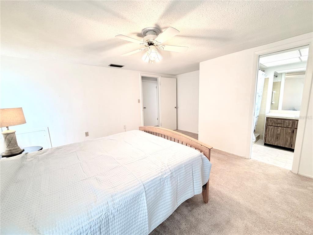 A bedroom with a bed, ceiling fan, and an attached bathroom with a vanity — 7016 CUTTY SARK DRIVE, PORT RICHEY, FL
