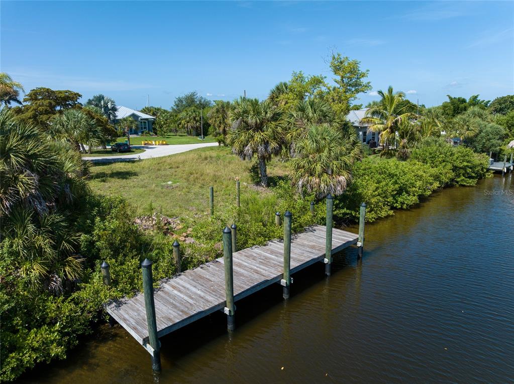 An aerial view of a wooden dock extending into a canal beside a grassy lot — 19188 NEW HAVEN COURT, PORT CHARLOTTE, FL