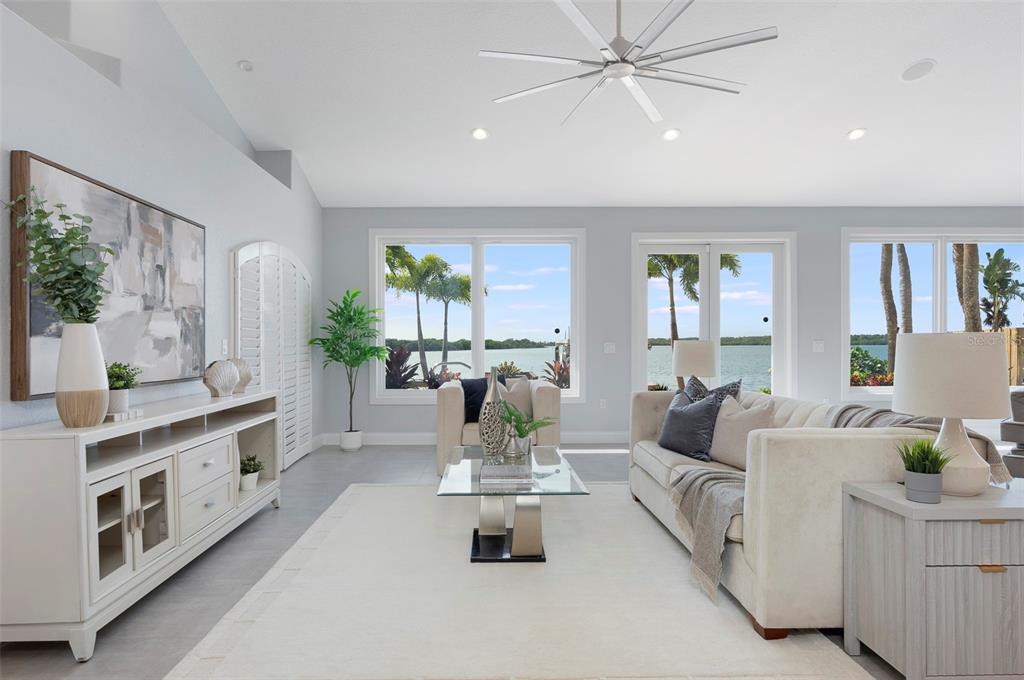 A bright living room features a white sofa, glass coffee table, and large waterfront windows — 8400 35TH AVENUE N, ST PETERSBURG, FL