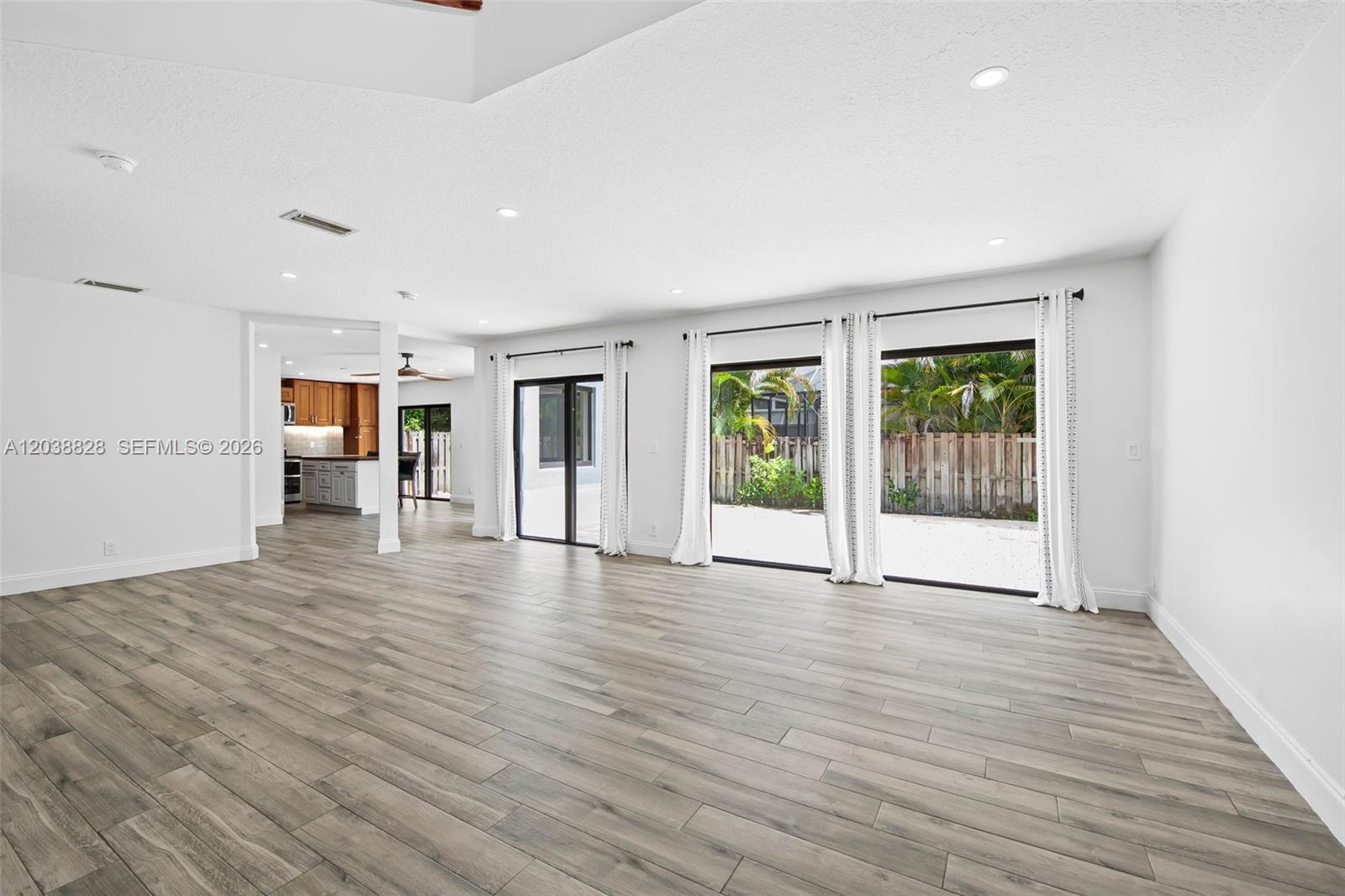 A spacious living room features light wood-look flooring, white walls, and large sliding glass doors — 11293 Rhapsody Rd # 0, Cooper City FL 33026, COOPER CITY, FL