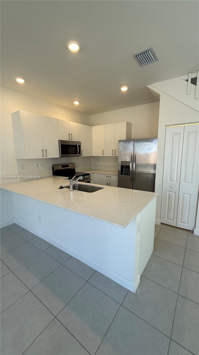 A kitchen features white cabinets, stainless steel appliances, and a light-colored quartz countertop island — 679 SE 13th St Cir, Homestead FL 33034, HOMESTEAD, FL