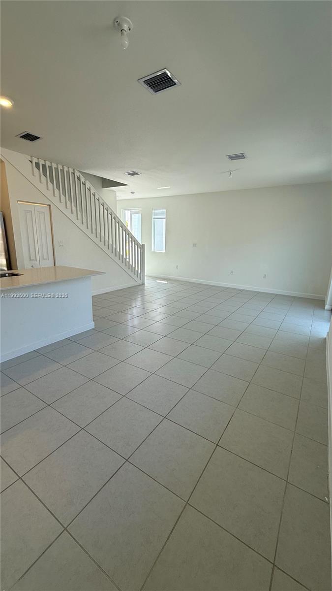 An open-concept living area features light tile flooring, a white staircase, and recessed lighting — 679 SE 13th St Cir, Homestead FL 33034, HOMESTEAD, FL