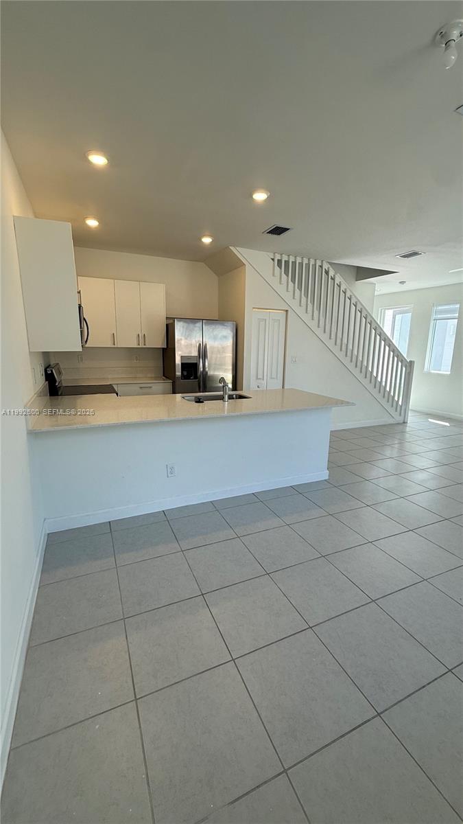 A kitchen with white cabinets, stainless steel appliances, and a breakfast bar overlooks a room — 679 SE 13th St Cir, Homestead FL 33034, HOMESTEAD, FL