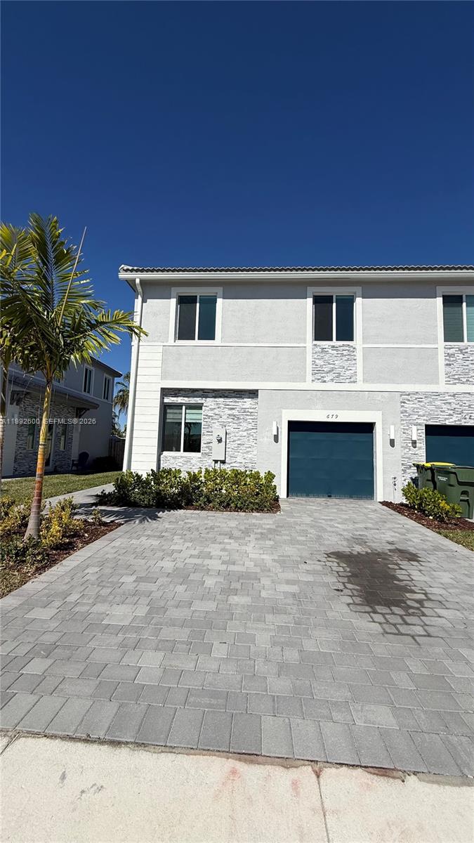 A two-story townhouse with a paved driveway, a blue garage door, and stone veneer accents — 679 SE 13th St Cir, Homestead FL 33034, HOMESTEAD, FL