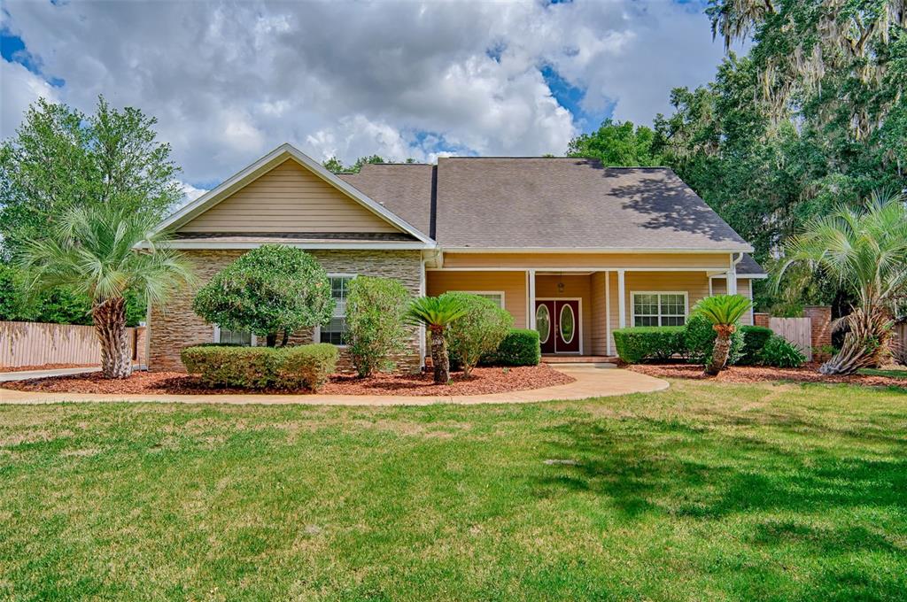 A single-story house with tan siding, stone accents, and a front walkway on a lawn — 12208 SW 9TH AVENUE, NEWBERRY, FL