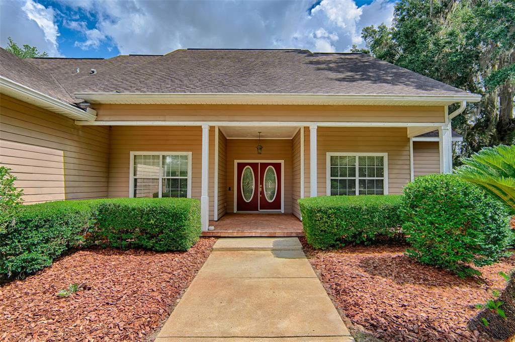 The exterior view shows a tan house with a concrete walkway leading to double doors — 12208 SW 9TH AVENUE, NEWBERRY, FL