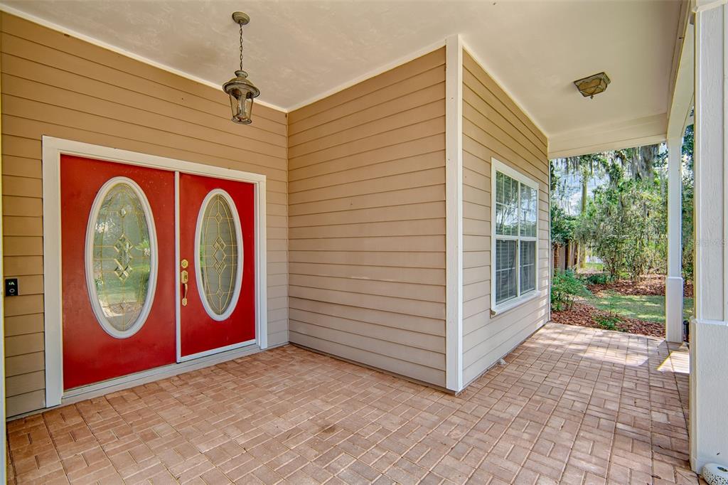 A covered brick porch features a bright red double front door and tan siding — 12208 SW 9TH AVENUE, NEWBERRY, FL