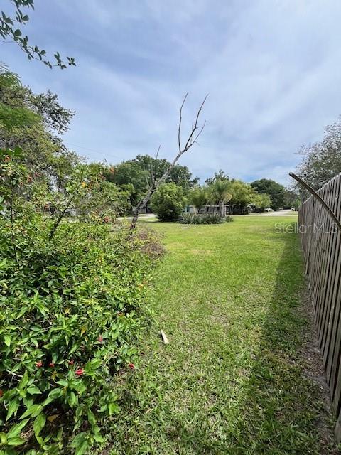 A grassy yard is bordered by a wooden fence and a large, leafy shrub — 4741 18TH STREET, ZEPHYRHILLS, FL