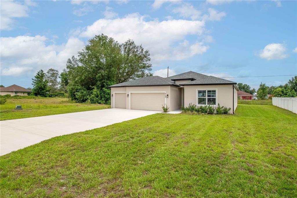 A single-story house with a beige exterior, a three-car garage, and a large grassy yard — 4780 SW 129TH PLACE, OCALA, FL