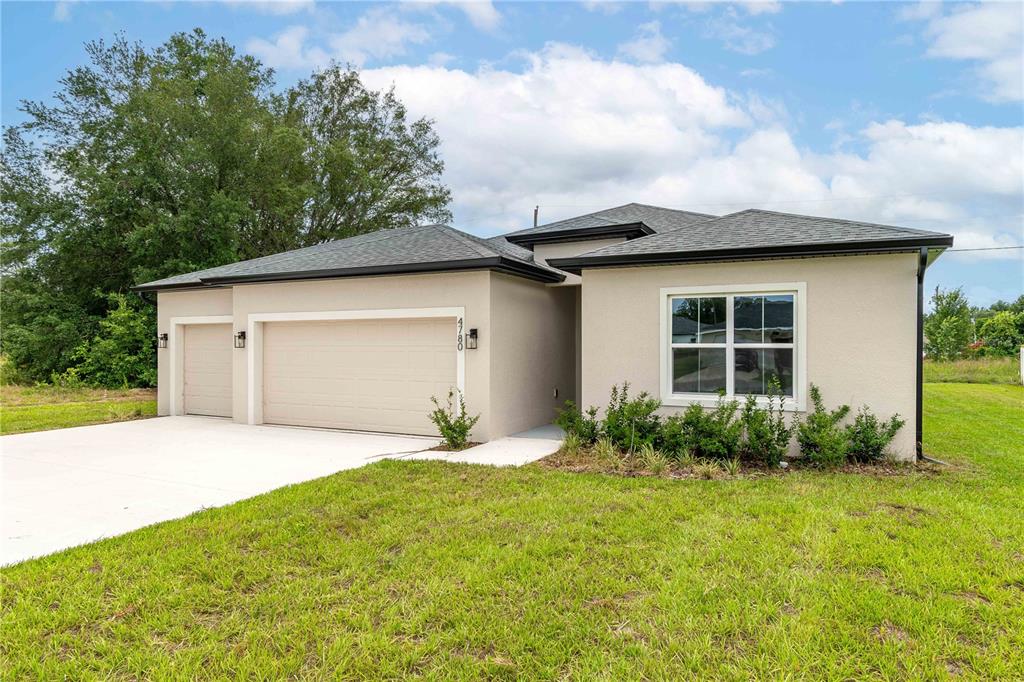 A single-story house with a beige stucco exterior, a three-car garage, and a grassy lawn — 4780 SW 129TH PLACE, OCALA, FL