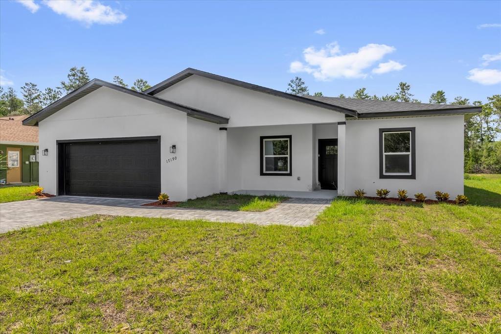 A modern, single-story white house with a black garage door and dark window trim — 17190 SW 44TH CIRCLE, OCALA, FL