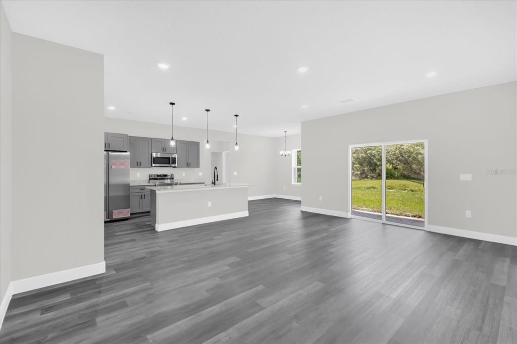 A modern open-concept kitchen and living area with gray flooring and sliding glass doors — 17190 SW 44TH CIRCLE, OCALA, FL