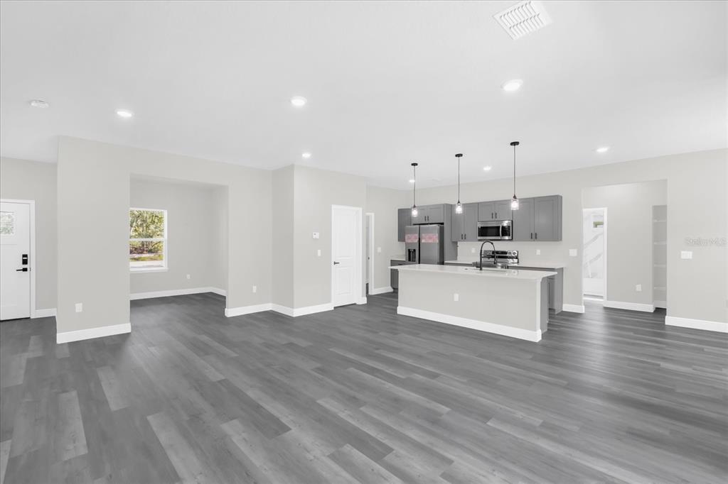 An open-concept kitchen and living area features gray cabinetry, a central island, and wood-look flooring — 17190 SW 44TH CIRCLE, OCALA, FL