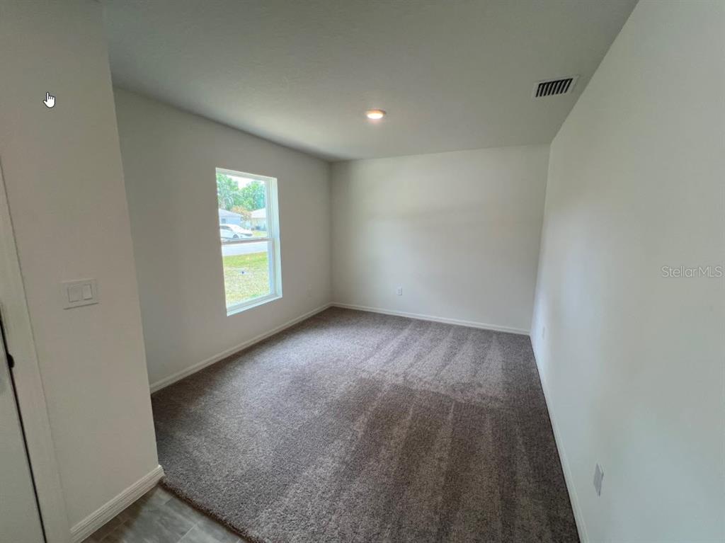 An empty bedroom features gray carpet, white walls, a single window, and a ceiling light — 25 RYDING LANE, PALM COAST, FL