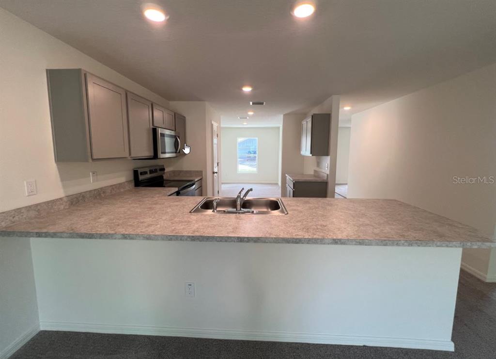 A kitchen features gray cabinets, laminate countertops, a double sink, and a breakfast bar — 25 RYDING LANE, PALM COAST, FL