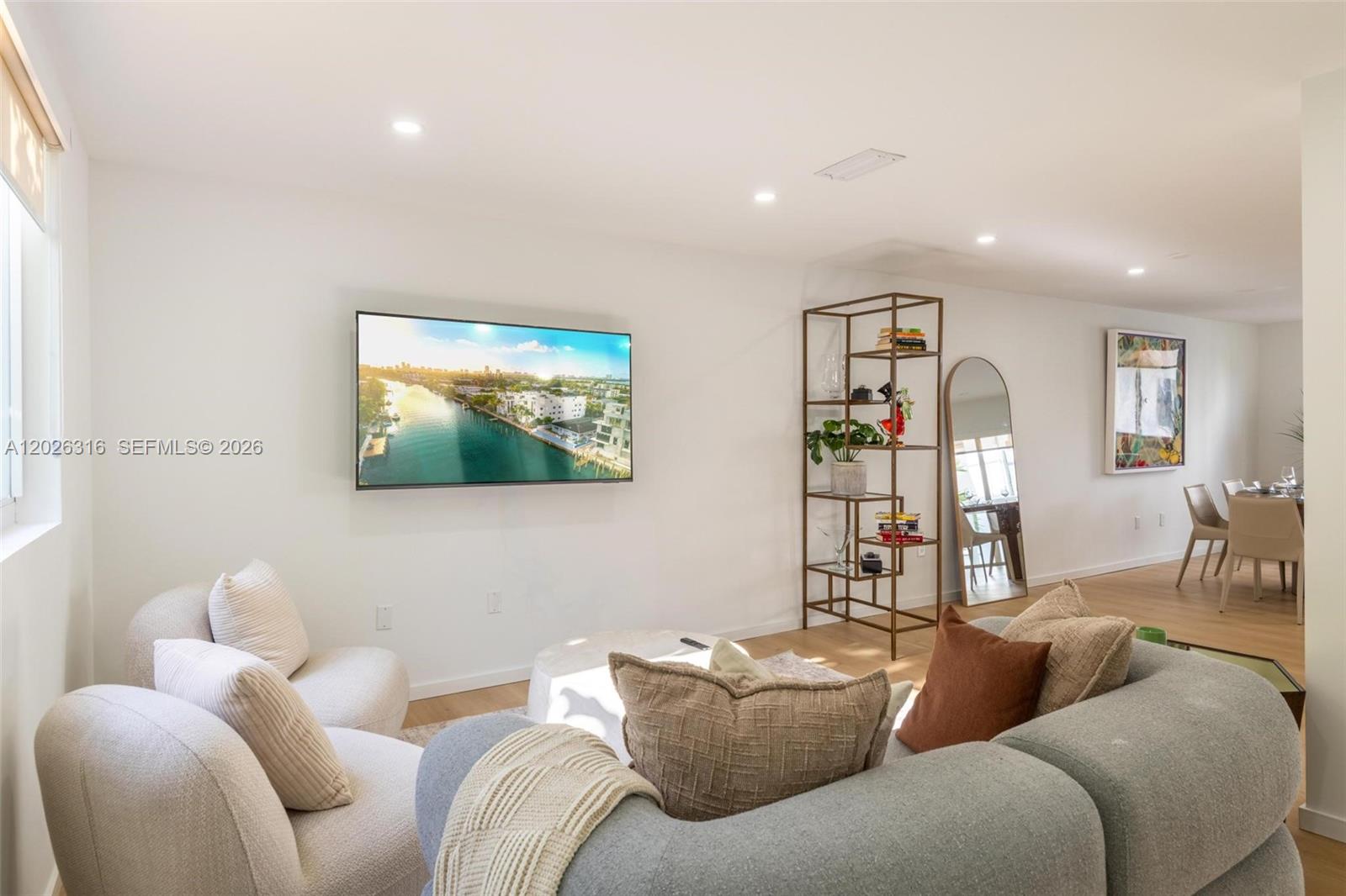 A living room features a wall-mounted television, a metal shelving unit, and a curved sofa — 1975 Calais Dr # 4, Miami Beach FL 33141, MIAMI BEACH, FL