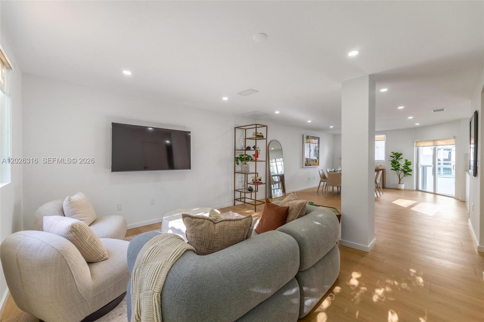 A living room with a grey sectional, white chairs, wall-mounted television, and adjacent dining area — 1975 Calais Dr # 4, Miami Beach FL 33141, MIAMI BEACH, FL