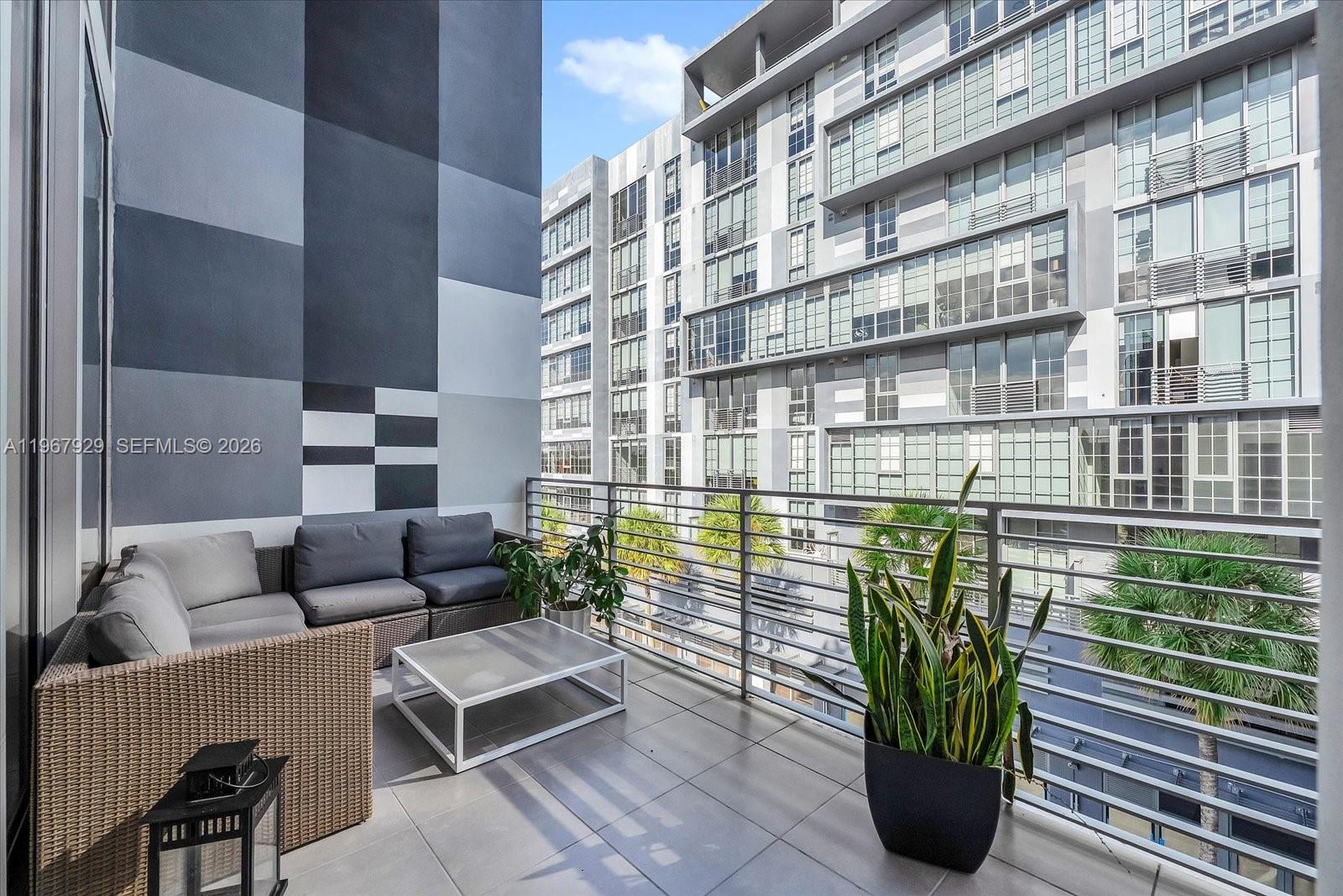 A balcony features a wicker sectional sofa, a coffee table, and a potted snake plant — 250 NW 24th St # 4A, Miami FL 33127, MIAMI, FL