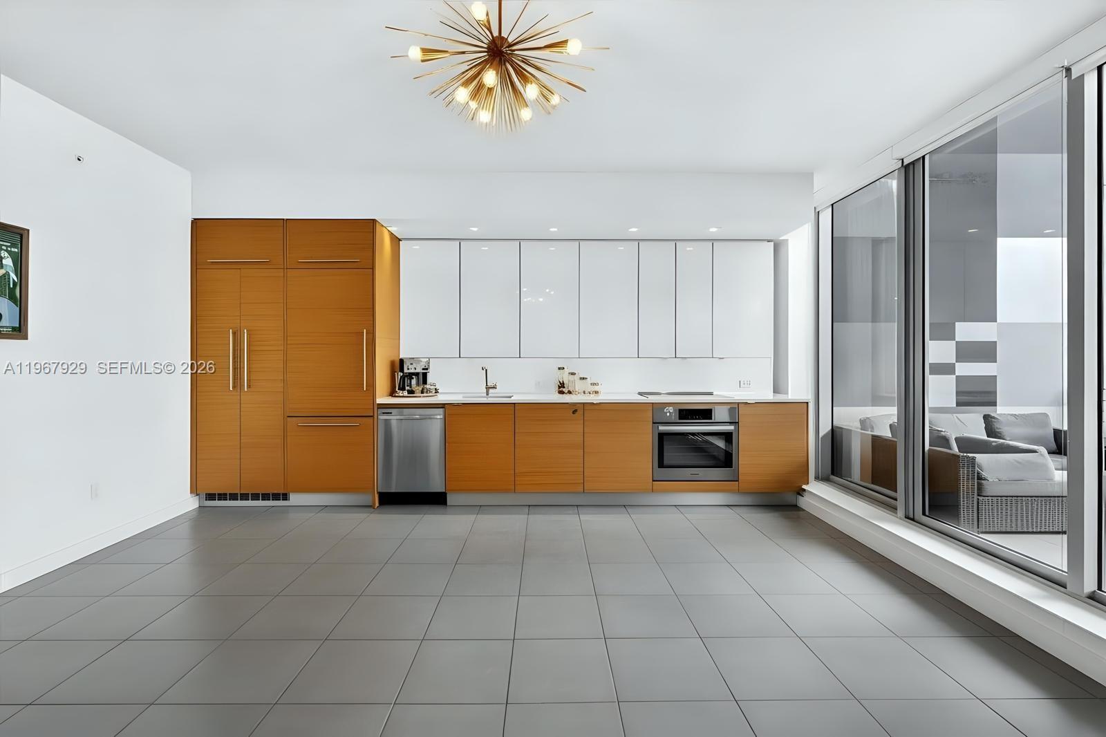 A modern kitchen features wood-toned lower cabinets, white upper cabinets, and large floor-to-ceiling windows — 250 NW 24th St # 4A, Miami FL 33127, MIAMI, FL
