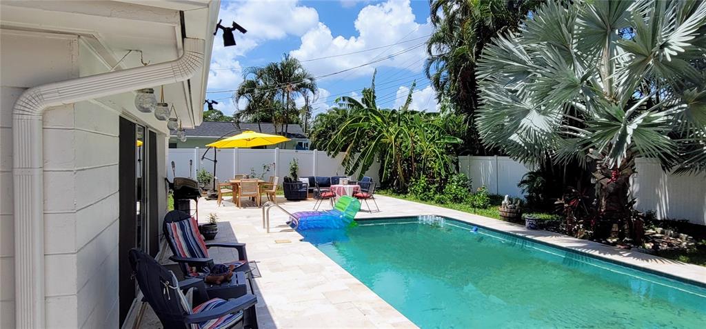 A backyard features a swimming pool, patio furniture, a yellow umbrella, and a large palm tree — 1279 86TH AVENUE N, ST PETERSBURG, FL