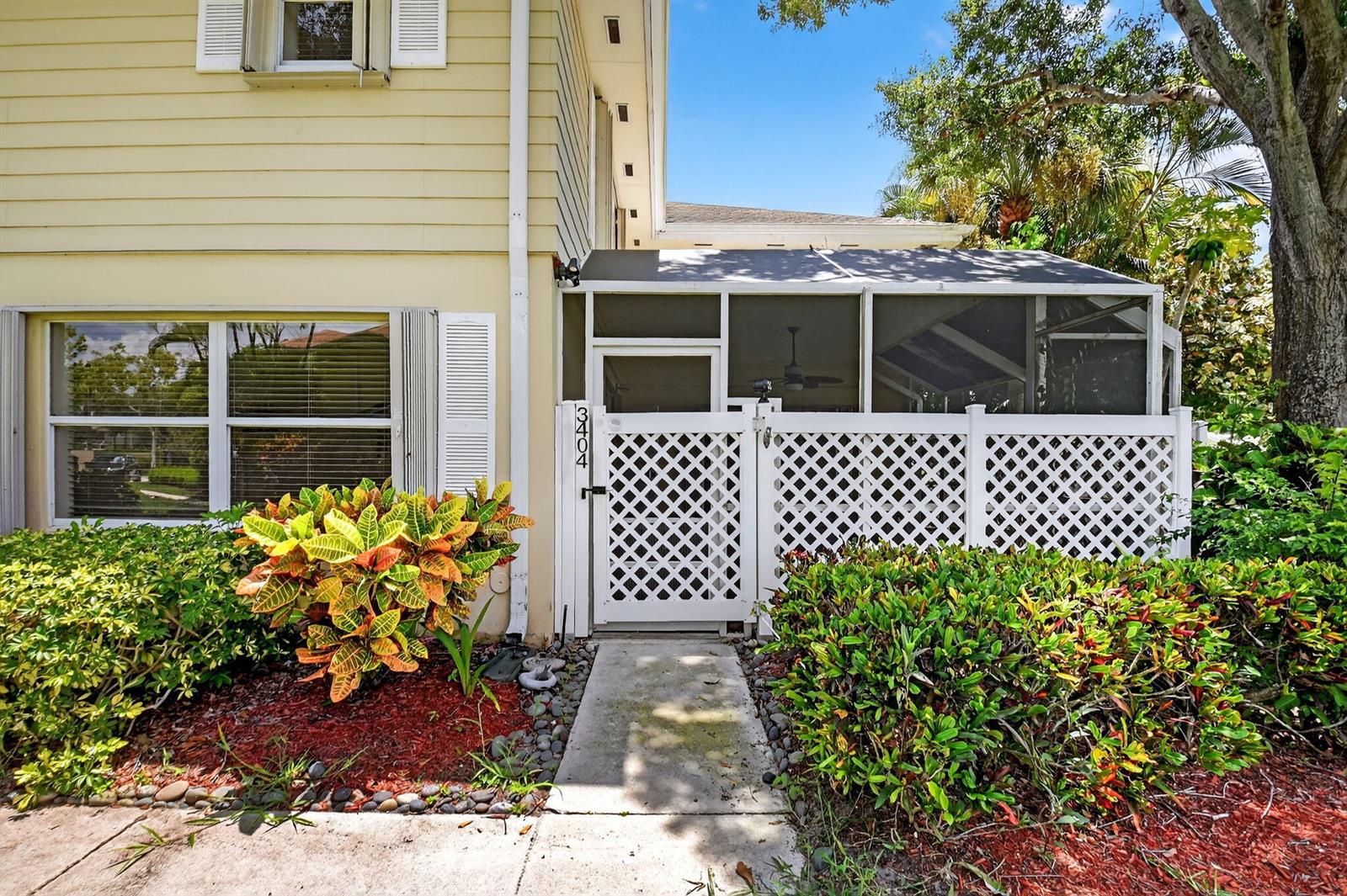 A yellow house exterior features a white lattice gate leading to a screened-in patio area — 3404 Hayden Court, Boynton Beach FL 33436, BOYNTON BEACH, FL