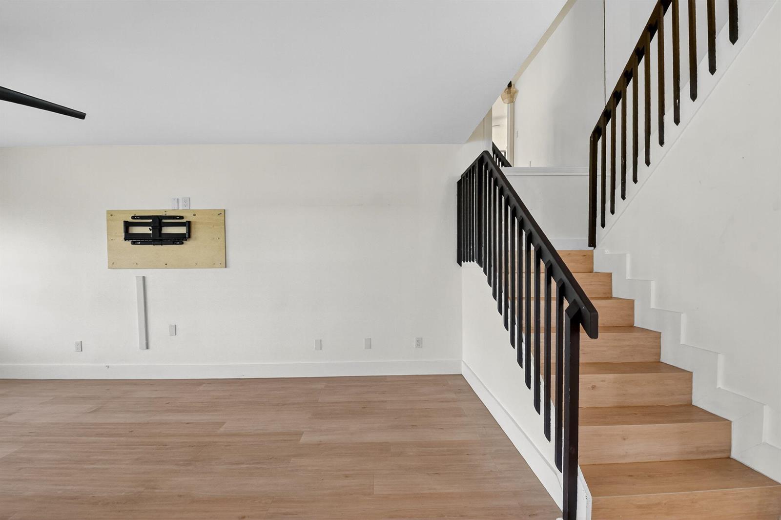 A living room with light wood flooring, white walls, a wall-mounted TV bracket, and stairs — 3404 Hayden Court, Boynton Beach FL 33436, BOYNTON BEACH, FL