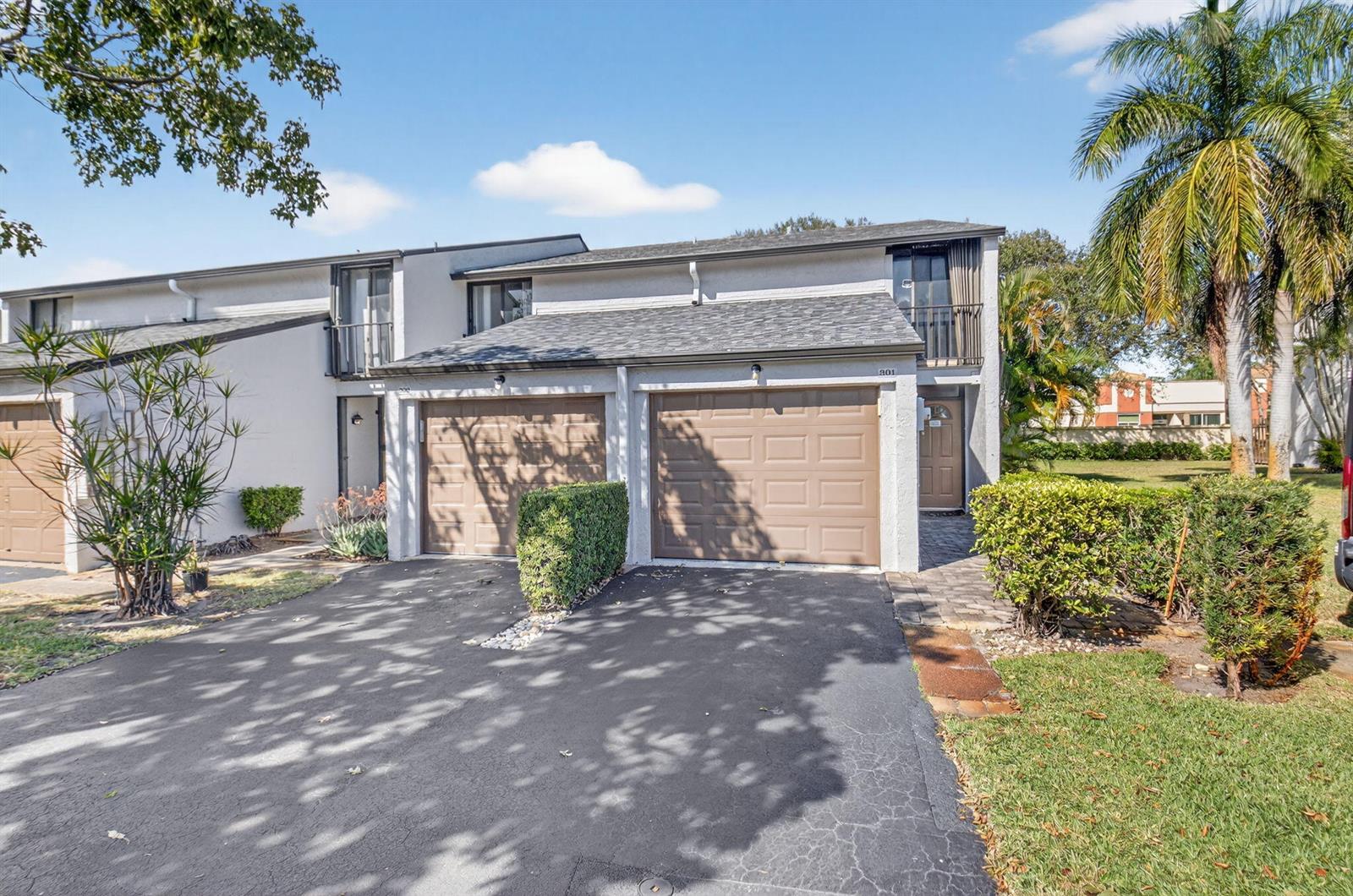 A two-story townhouse exterior features two brown garage doors, a paved driveway, and palm trees — 4761 NW 2nd Avenue # 301, Boca Raton FL 33431, BOCA RATON, FL