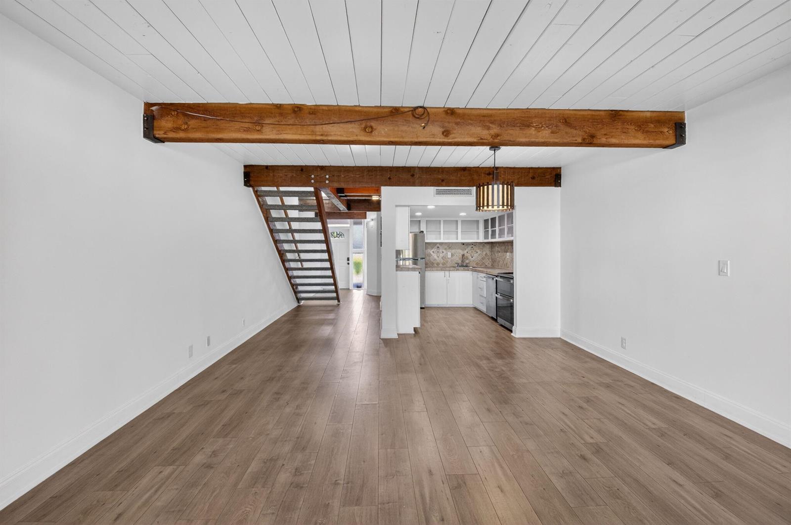 An open-concept living area features wood-plank flooring, exposed ceiling beams, and a staircase — 4761 NW 2nd Avenue # 301, Boca Raton FL 33431, BOCA RATON, FL