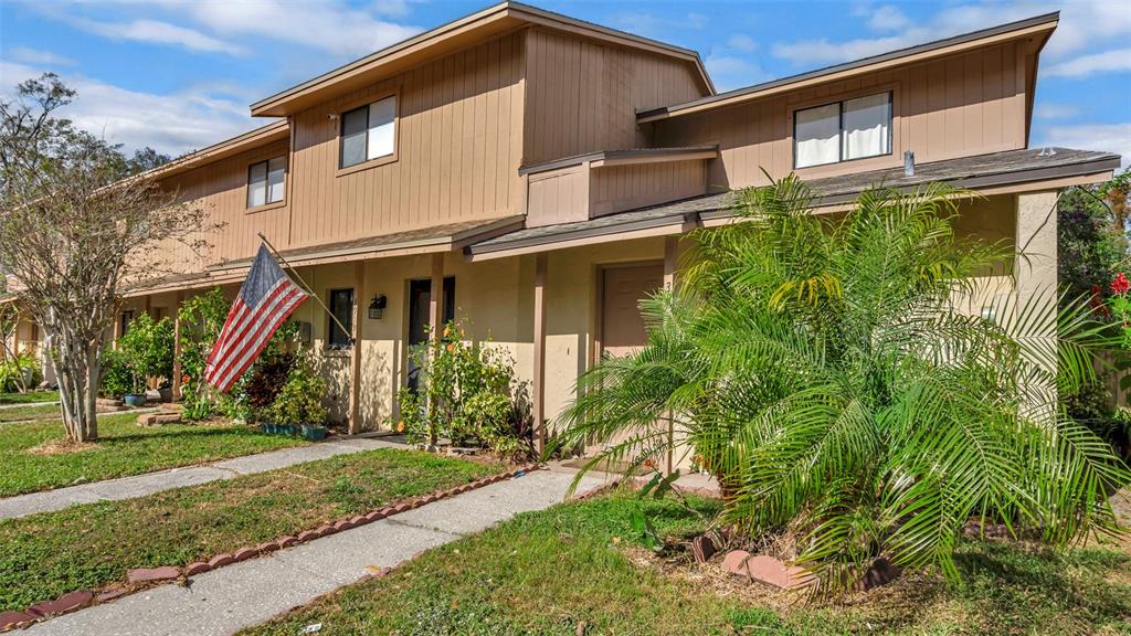 A two-story tan townhouse exterior features a front walkway, an American flag, and landscaping — 3913 OAK LIMB COURT, TAMPA, FL