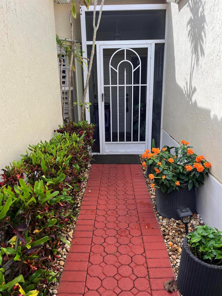 A red brick walkway leads to a white screen door framed by potted plants — 6108 Petunia Road, Delray Beach FL 33484, DELRAY BEACH, FL