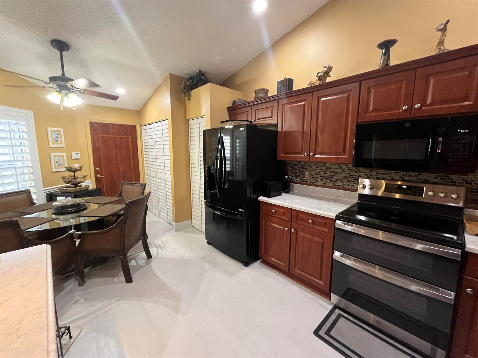 A kitchen features dark wood cabinets, black appliances, a dining table, and light-colored flooring — 6108 Petunia Road, Delray Beach FL 33484, DELRAY BEACH, FL