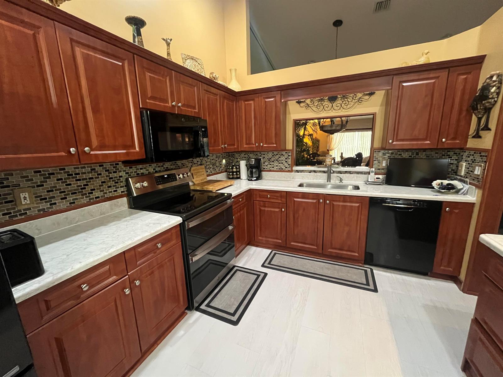 A kitchen features cherry wood cabinets, black appliances, a tiled backsplash, and light-colored countertops — 6108 Petunia Road, Delray Beach FL 33484, DELRAY BEACH, FL