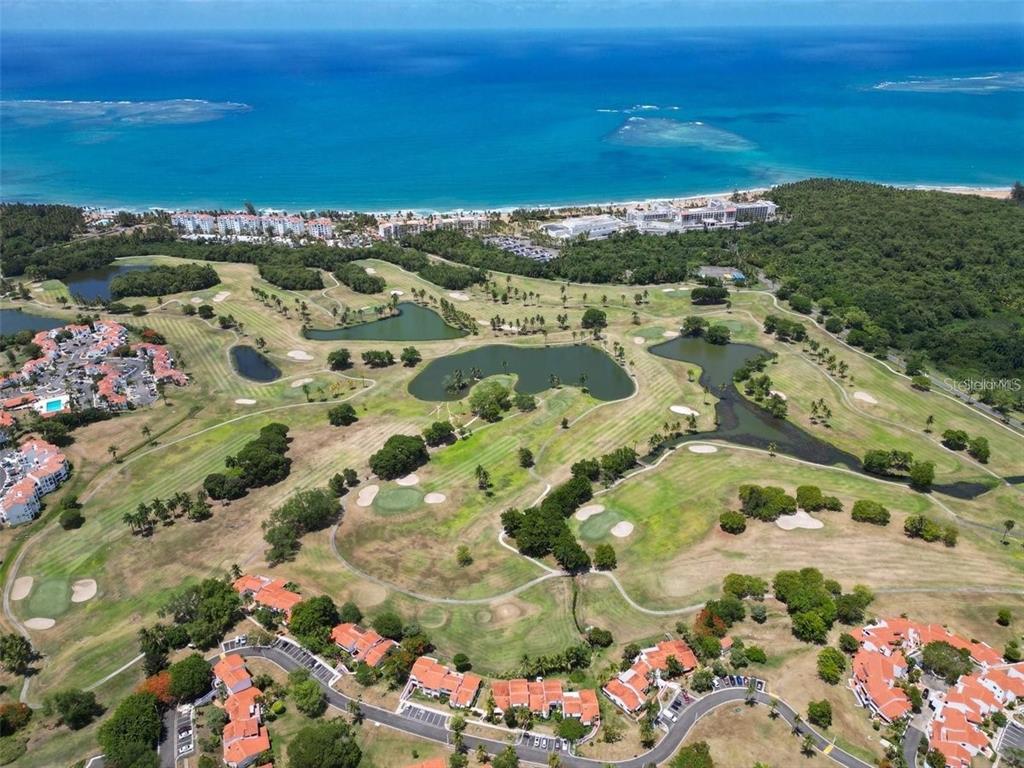 An aerial view shows a golf course with several ponds, surrounding residential buildings, and the ocean — 6000 RIO MAR BOULEVARD, RIO GRANDE, PR