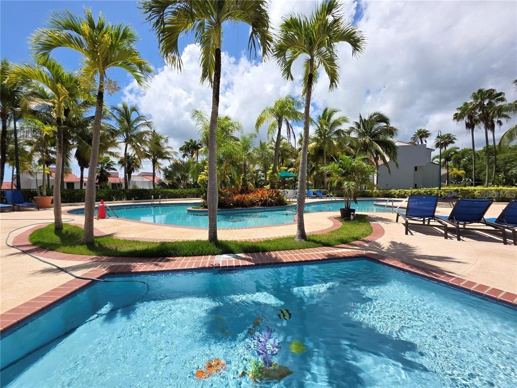 A swimming pool with decorative floor tiles sits in front of a larger community pool — 6000 RIO MAR BOULEVARD, RIO GRANDE, PR