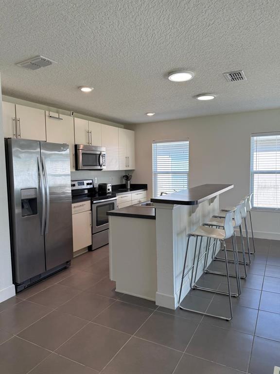 A kitchen features stainless steel appliances, white cabinetry, dark countertops, and a breakfast bar with stools — 3230 BAYOU LANE, TAVARES, FL